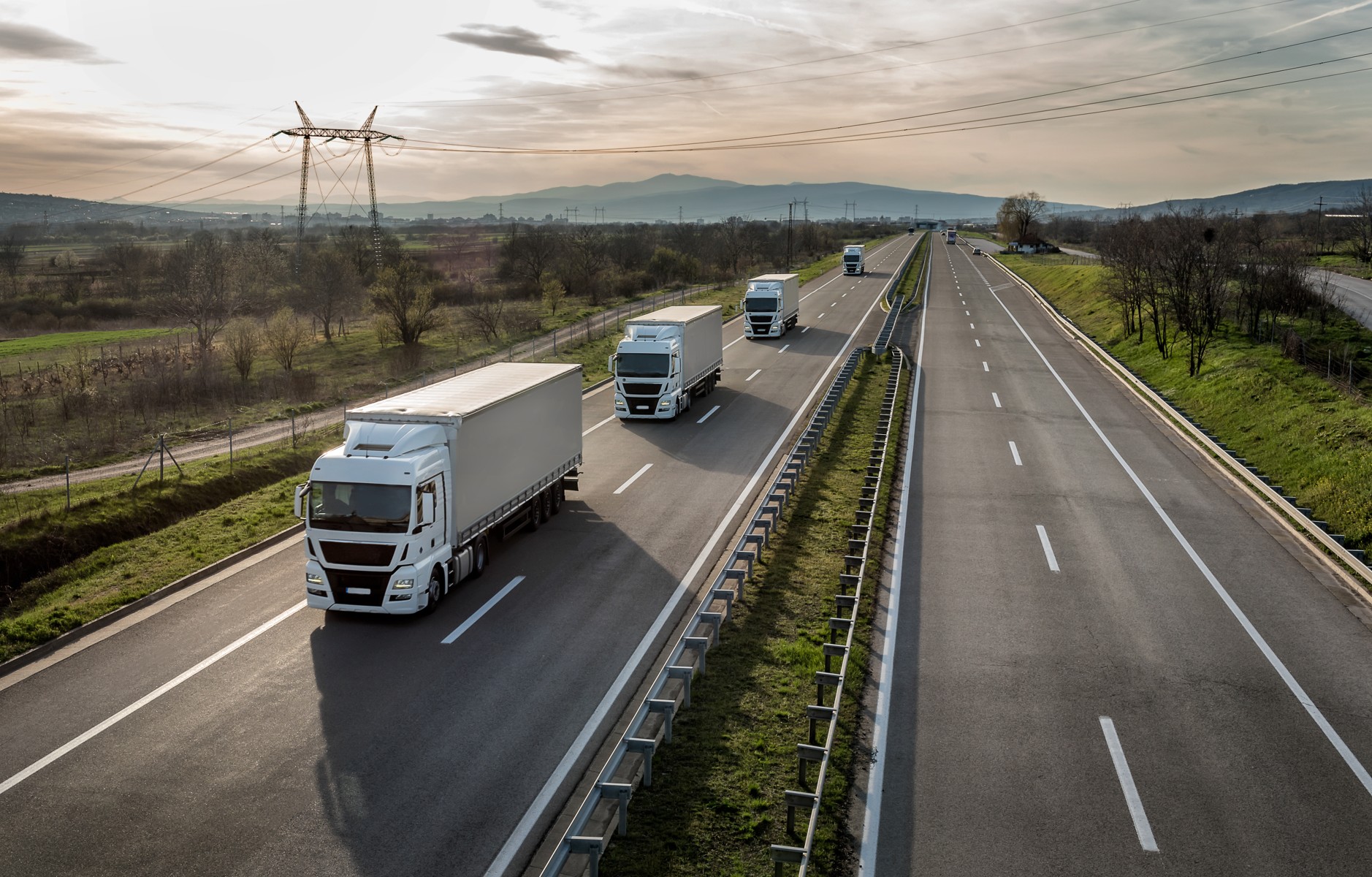 Convoy of white delivery trucks on a South African highway at dusk, illustrating goods in transit insurance for cargo on the road.